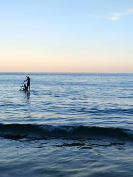 silhouette of a man and a woman sailing on a supboard in the sea at sunset.