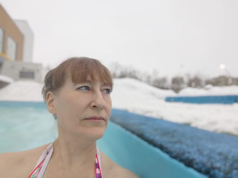 Adult mature woman takes selfie in a pool with warm hot termal mineral water in winter and white snow around. Wellness center and the concept of health care. Travel, recreation, medicine and rest