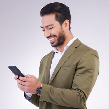 Business man, smile and phone for communication in studio while typing and networking on gray background. Asian male entrepreneur with smartphone for email, online chat or marketing on social media.