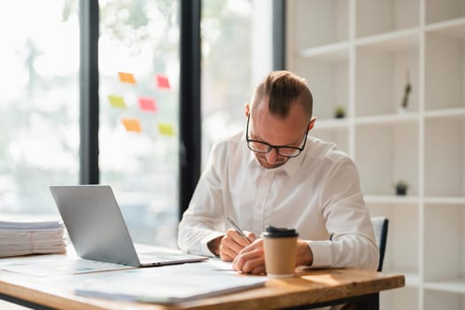 business man in casual making notes in notepad while sitting in his office.