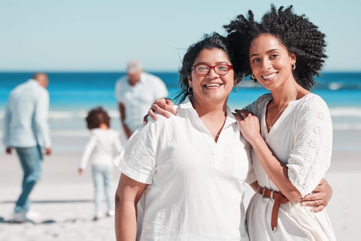Portrait, nature with a mother and daughter on the beach during summer while their family play in the background. Love, smile or summer with a senior woman and adult child bonding outdoor together.