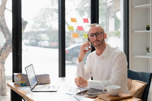 Happy handsome businessman working on laptop and having phone conversation, in office.