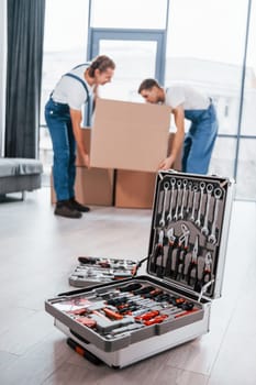 Case with equipment. Two young movers in blue uniform working indoors in the room.