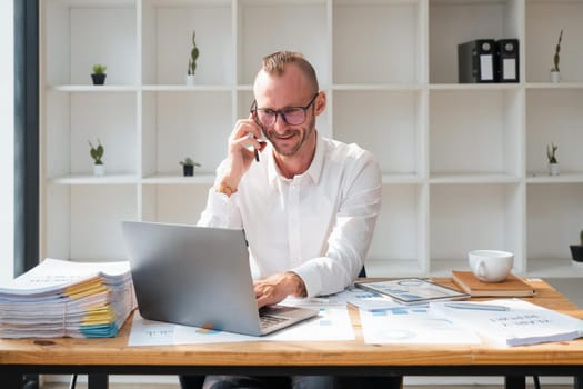 businessman handsome talking to the phone at workplace and using laptop in office.