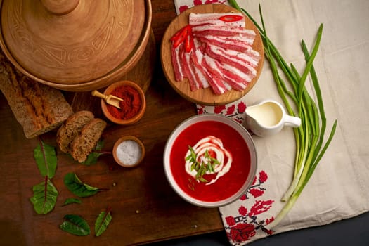 Traditional Ukrainian borsht, red vegetable soup or borscht with smetana on wooden background. Slavic dish with cabbage, beets, tomatoes Traditional Ukrainian towel along with garlic, bread and salt. Top view of a wooden tray on a black background on which lies Ukrainian food with spices