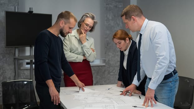 Four business people review and discuss blueprints. Designers engineers at a meeting