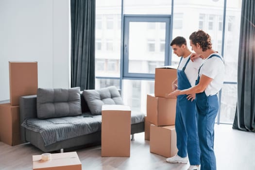 Two young movers in blue uniform working indoors in the room.