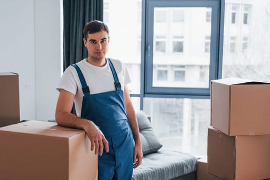 Young male mover in blue uniform works indoors in the room.