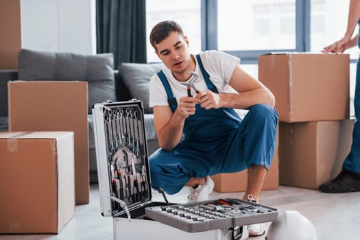 Young male mover in blue uniform works indoors in the room.