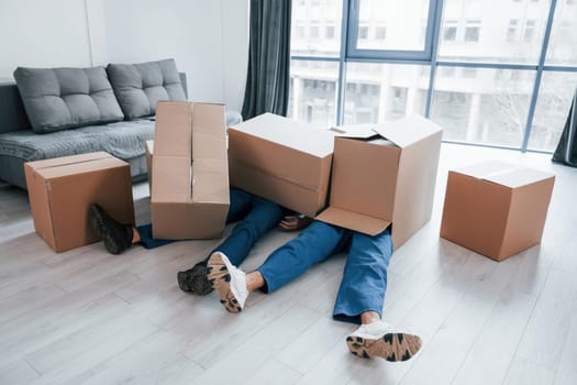 Two young male movers in blue uniform lying down on the floor with boxes.