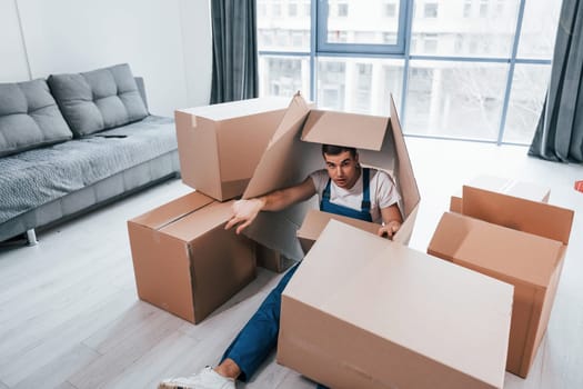 Young male mover in blue uniform lying down on the floor with boxes.