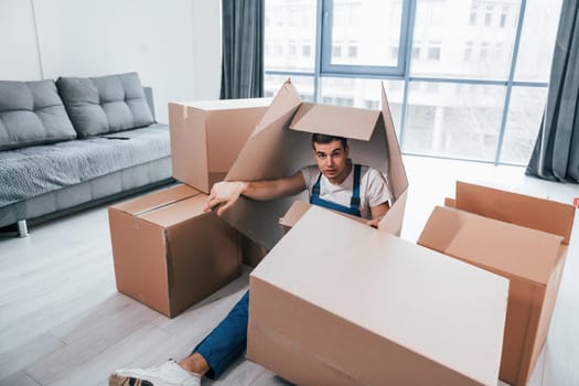 Young male mover in blue uniform lying down on the floor with boxes.