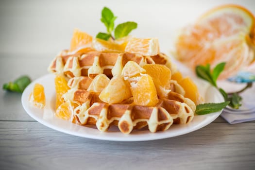 Cooked sweet Belgian waffles with oranges on a wooden table.