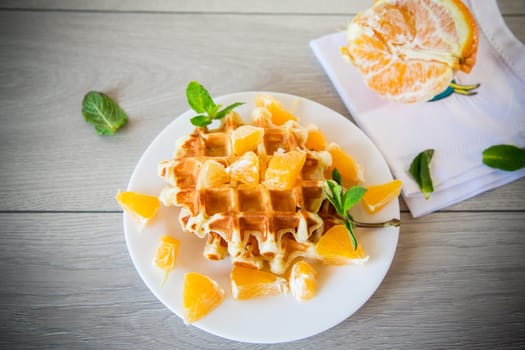 Cooked sweet Belgian waffles with oranges on a wooden table.