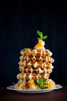 Cooked sweet Belgian waffles with oranges on a black background