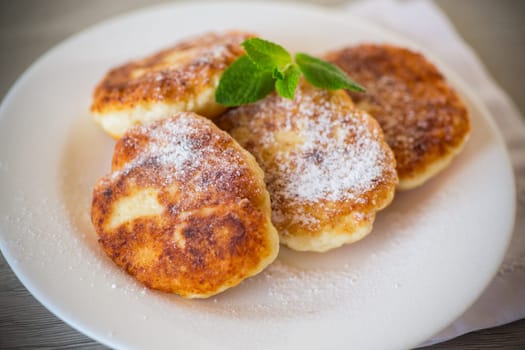 Sweet cooked cheesecakes in powdered sugar in a plate on the table.