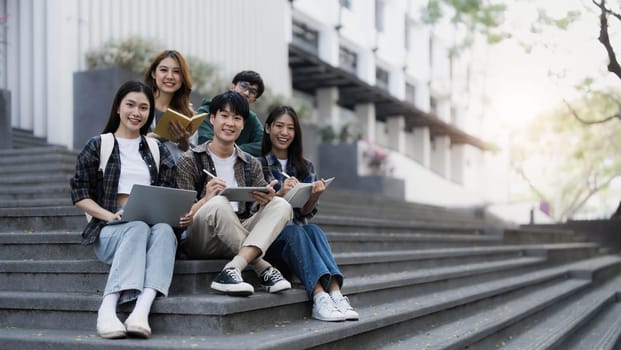 Group of cheerful Asian college students sitting on stairs, showing fists, celebrating triumph..