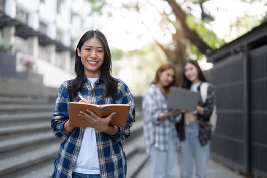 young happy attractive asian student smiling and looking at camera with friends on outdoor university background. Asian woman in self future education or personalized learning concept...