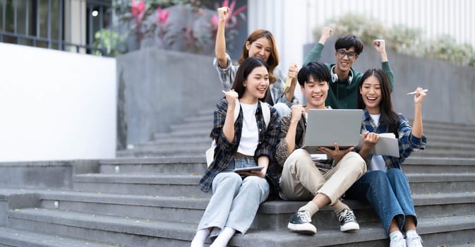 Group of cheerful Asian college students sitting on stairs, showing fists, celebrating triumph..