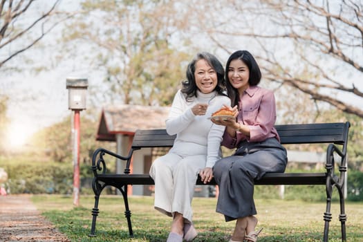 Happy adult granddaughter and senior grandmother having fun enjoying talk sit with green nature. in park..