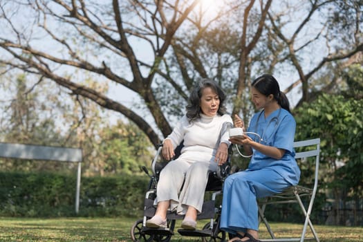 Female nurse doing blood pressure measurement of a senior woman patient. Doctor checking blood pressure of an elderly woman at garden home. Female caregiver and senior woman together