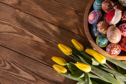 Hand-painted Easter eggs stacked on top of each other in a wooden bowl. Easter decoration as a base for your own composition or graphic inscriptions.