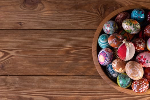 Top view of a wooden bowl filled with colorful Easter eggs. Easter composition with a view to adding graphic elements on your own.