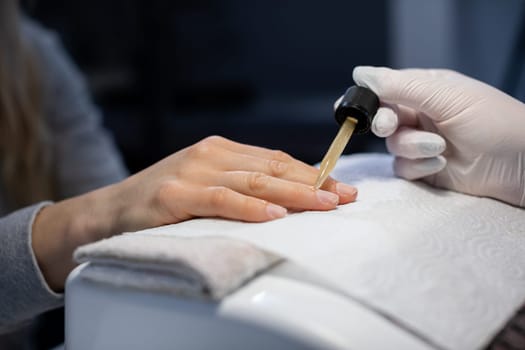 The professional nourishes the client's nails with cosmetic oil. The beautician wears disposable nitrile gloves. Maintaining the rules of hygiene in the beauty salon.