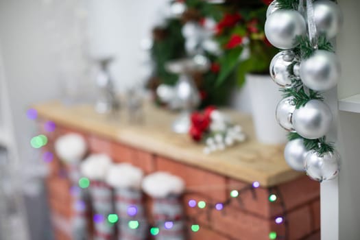 Silver baubles on spruce twigs and decorated fireplace in background.