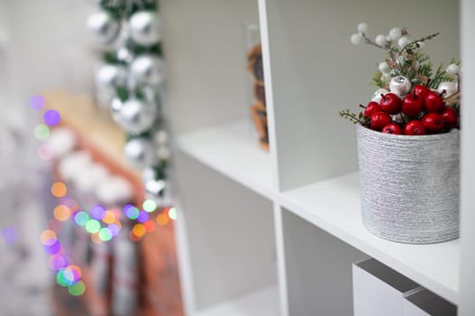 White cabinet with shelves and silver pot with red and white decorations. Brick fire place in background.
