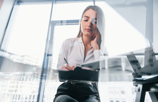 Busy day. Young woman in white formal clothes is indoors in the modern office.