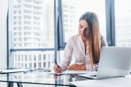 Busy day. Young woman in white formal clothes is indoors in the modern office.