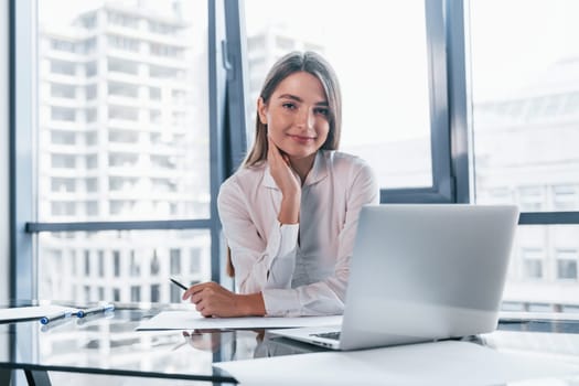 Young woman in white formal clothes is indoors in the modern office.