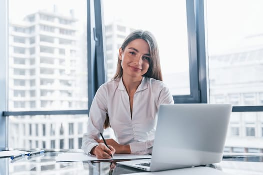 Young woman in white formal clothes is indoors in the modern office.