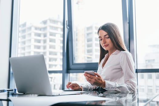 Busy day. Young woman in white formal clothes is indoors in the modern office.