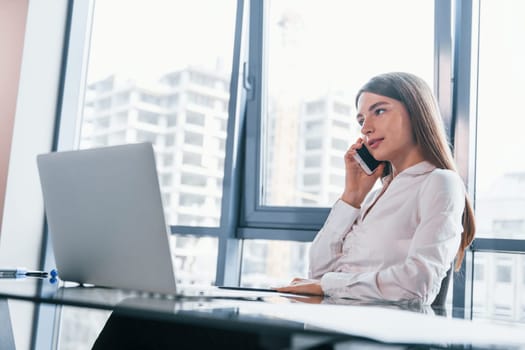 Busy day. Young woman in white formal clothes is indoors in the modern office.