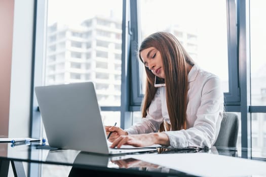 Busy day. Young woman in white formal clothes is indoors in the modern office.