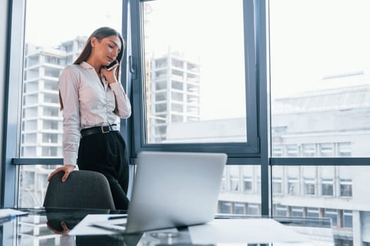 Young woman in white formal clothes is indoors in the modern office.