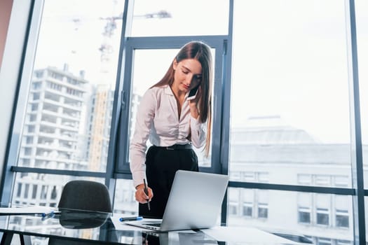Young woman in white formal clothes is indoors in the modern office.