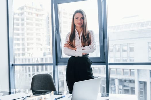 Young woman in white formal clothes is indoors in the modern office.