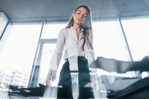 Busy day. Young woman in white formal clothes is indoors in the modern office.