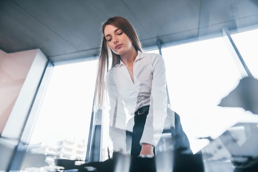 View from below. Young woman in white formal clothes is indoors in the modern office.