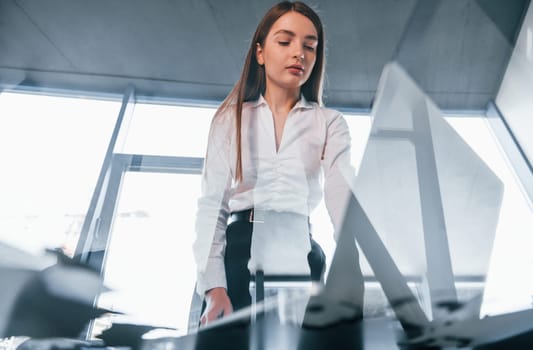 View from below. Young woman in white formal clothes is indoors in the modern office.