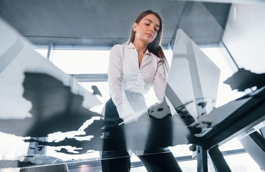 View from below. Young woman in white formal clothes is indoors in the modern office.