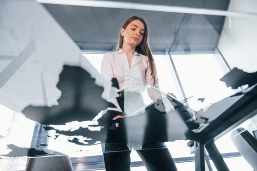View from below. Young woman in white formal clothes is indoors in the modern office.