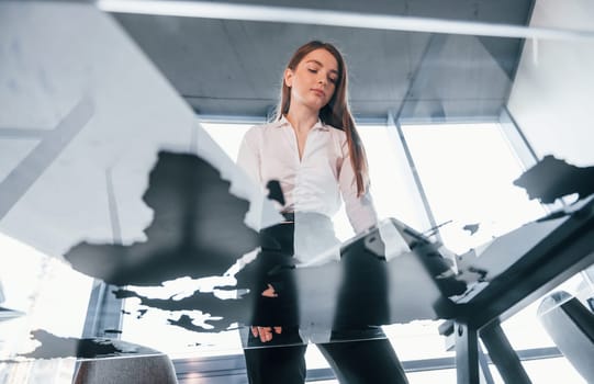 View from below. Young woman in white formal clothes is indoors in the modern office.