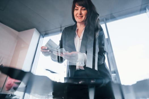 Woman in black formal clothes is indoors in the modern office.