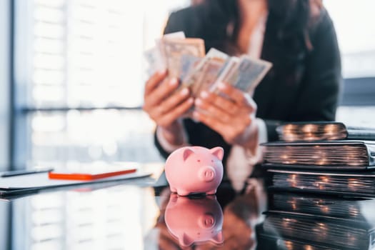 With currency. Woman in black formal clothes is indoors in the modern office.
