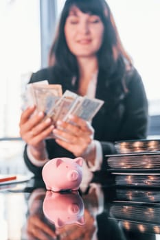With currency. Woman in black formal clothes is indoors in the modern office.