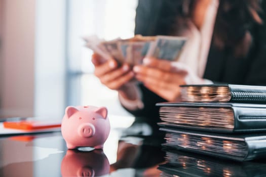 With currency. Woman in black formal clothes is indoors in the modern office.